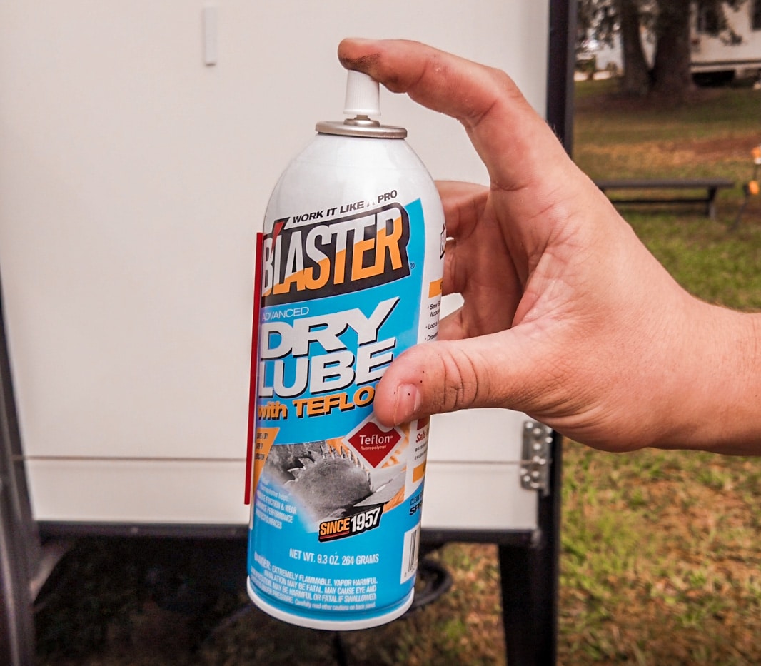 Hand holding Blaster Dry Lube with Teflon in front of an RV slide out.
