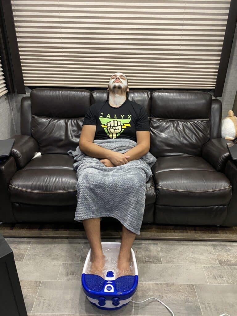 man soaking feet in spa and wearing face mask