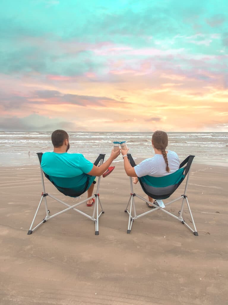 Couple in chairs on beach drinking coffee at sunrise