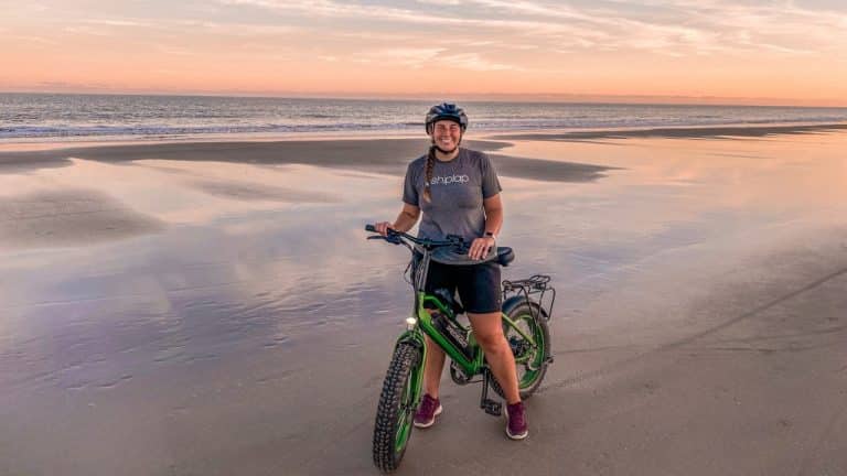 Woman with an e-bike on the beach at sunset