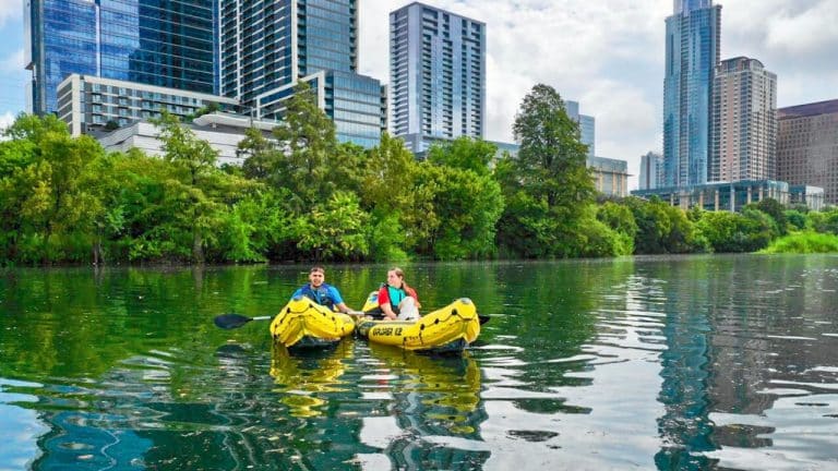 Two yellow inflatable kayaks on the river with city landscape in background