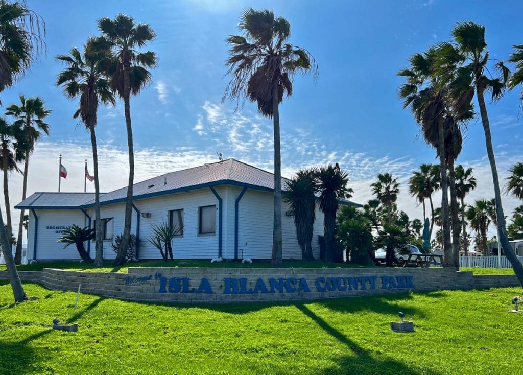 Isla Blanca RV Park welcome building surrounded by palm trees.