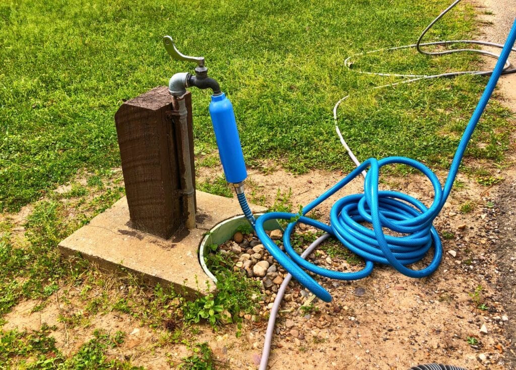 Blue RV water hose is hooked up to a water spigot with a Camco TastePure water filter connected to the hose and water spigot.