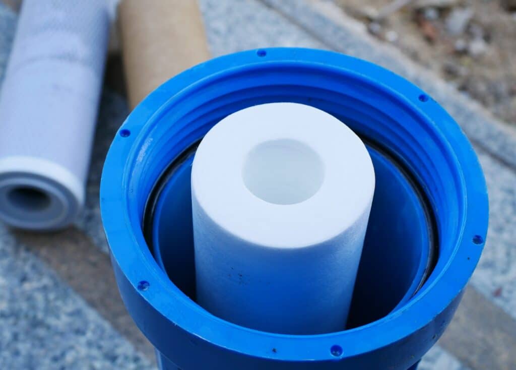 New water filter in a blue canister. Old, already used filters are laying on the ground in the background of the photo.