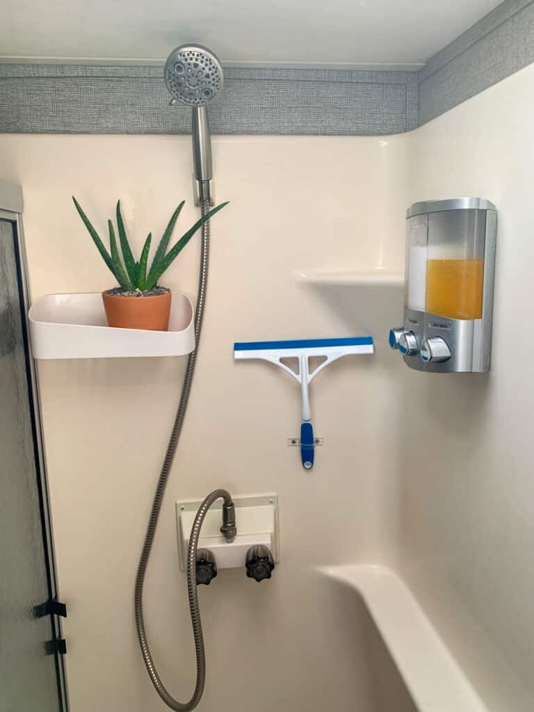 An aloe vera plant is potted in a terra cotta pot sitting on a floating white shelf inside a bathroom.