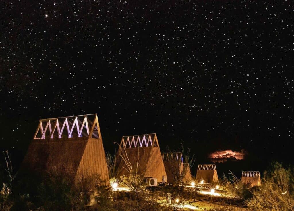 5 wooden A-frame "stargazers" at the Ocotillos Village are illuminated under a dark night sky filled with stars. 
