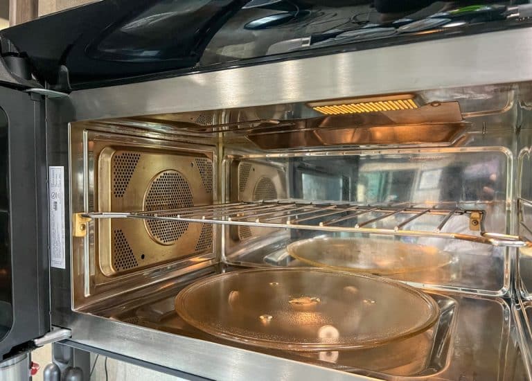 The inside of a RV microwave convection oven. The walls are a shiny metal and the microwave contains a shelf for a rack in the middle. On the bottom is a glass plate on a turntable.