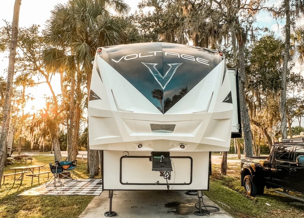 Dutchmen Voltage fifth wheel parked under some palm trees as the sun is setting.