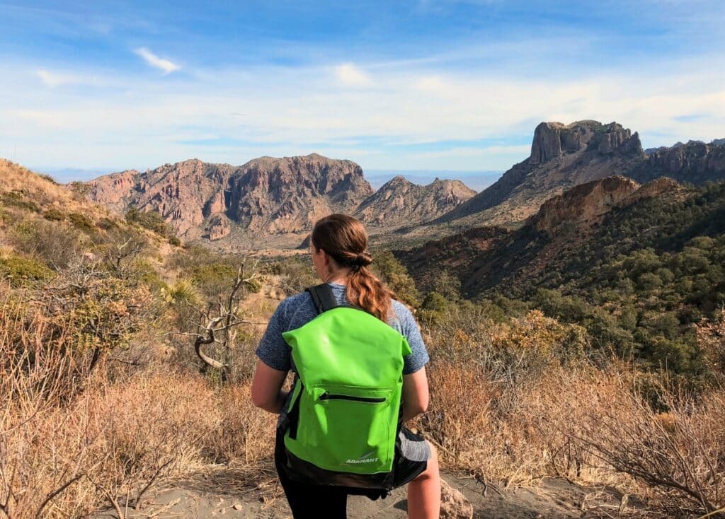 Woman wearing a bright green dry backpack stops to take in the mountain views in Big Bend National Park.