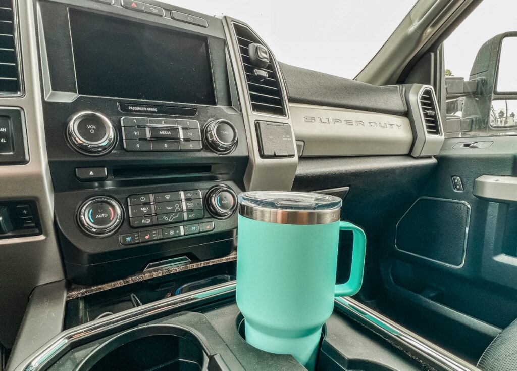 A teal Yeti tumbler with a handle sits in a cup holder inside a Ford F350 Super Duty. 