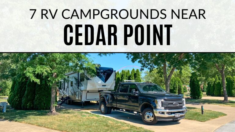 A white fifth wheel and black pickup truck are parked in an RV site at the Cedar Point RV Campground. In the background a roller coaster peaks out above the trees. Text on the image says "7 RV Campgrounds Near Cedar Point".