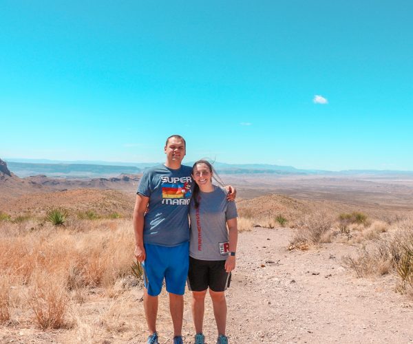 A man and a woman pose for a picture on a sunny day at the Sotol Vista Overlook. Santa Elena Canyon can be spotted way off in the distance.