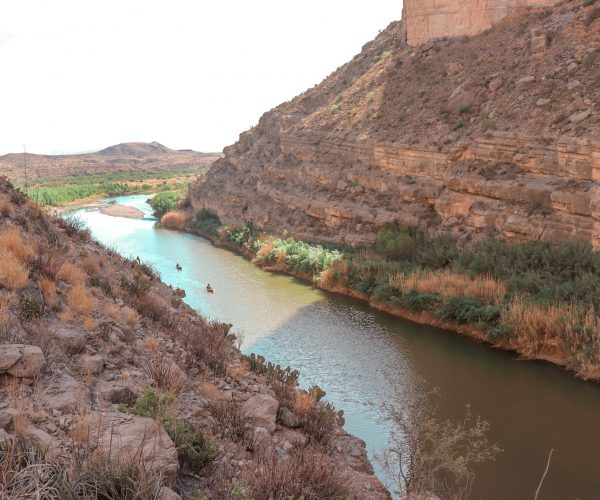 The photo looks down upon the Rio Grande from up on the Santa Elena Canyon Trail. In the distance, two canoes are paddling into the mouth of the canyon.