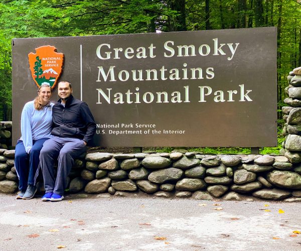 Couple sitting in front of Great Smoky Mountains National Park sign
