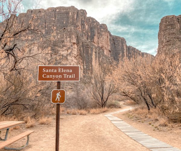 Brown National Park Santa Elena Canyon Trailhead Sign in front of the canyon. To the right of the sign a wooden boardwalk winds its way to the river.