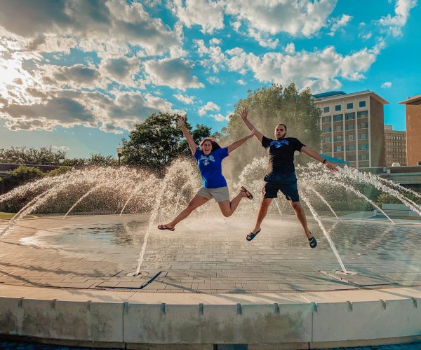 Man and woman jumping for joy in front of fountain at Indiana State University.