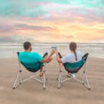 Couple in chairs on beach drinking coffee at sunrise