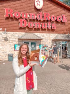 Woman holding Texas sized donut in front of Round Rock Donuts