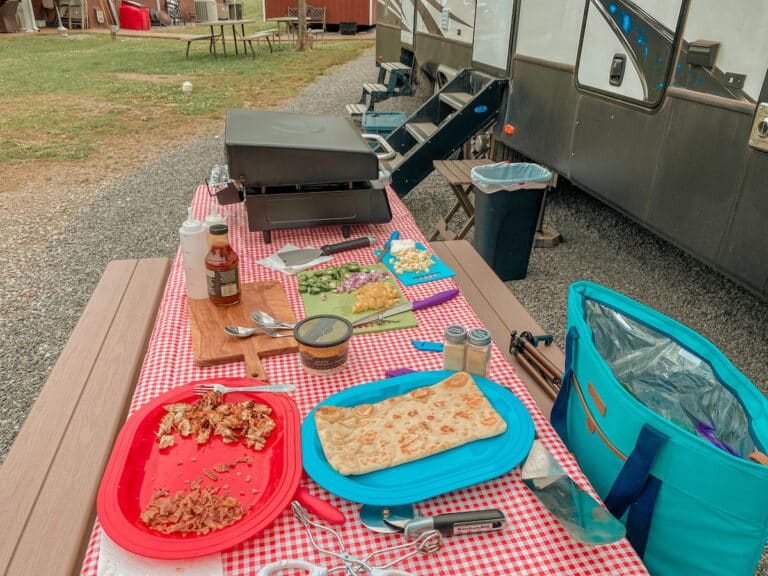 Picnic table with Blackstone Griddle and ingredients laid out for flatbread pizzas. RV in background.