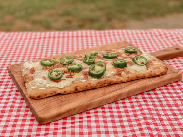 Jalapeno Popper pizza on a cutting board sitting on a picnic table with checkered table cloth