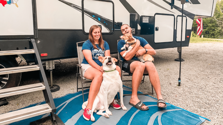 Couple sitting outside of their fifth wheel RV with their 2 dogs.