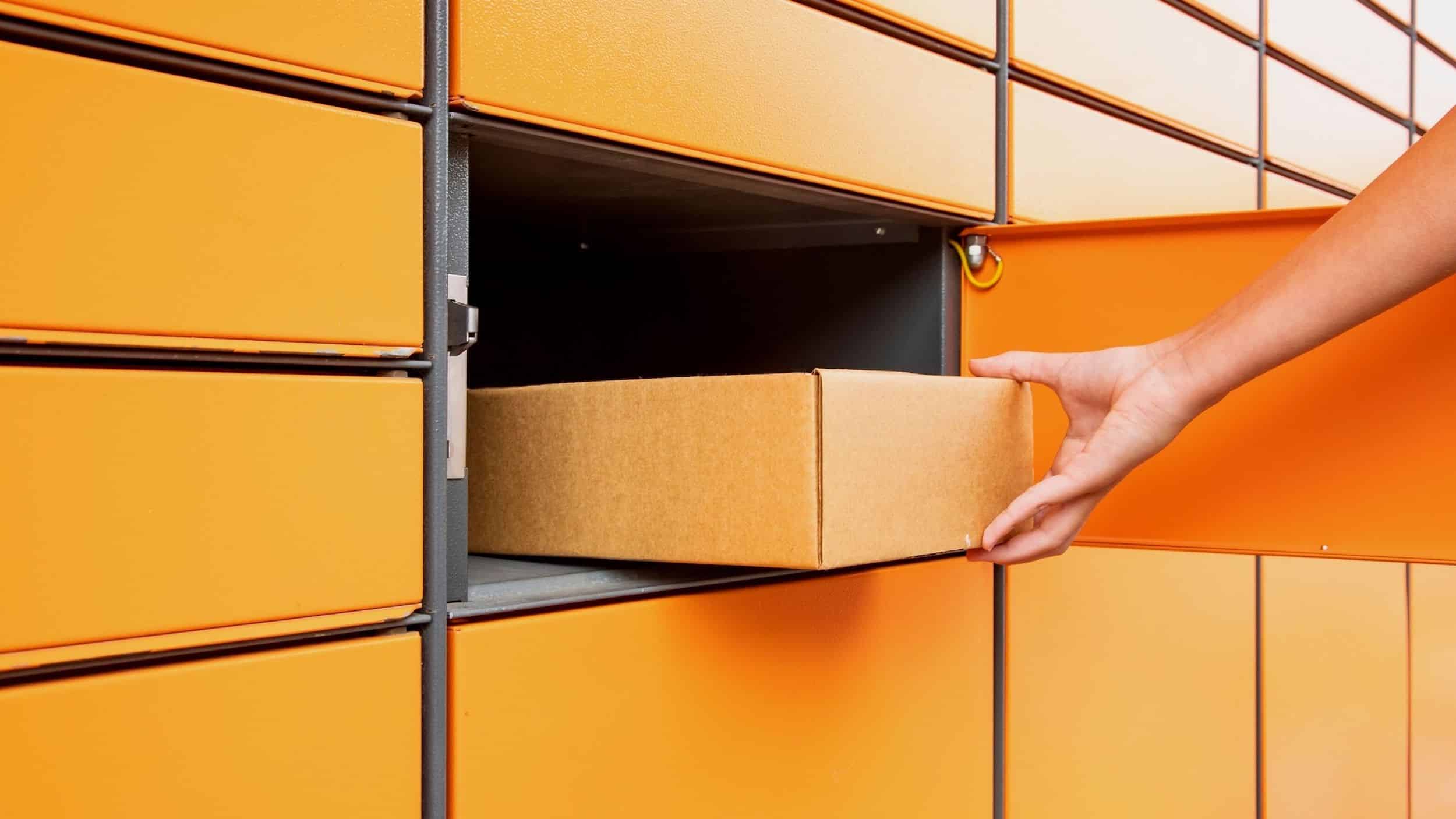 Orange amazon package lockers with one open and hand grabbing box.
