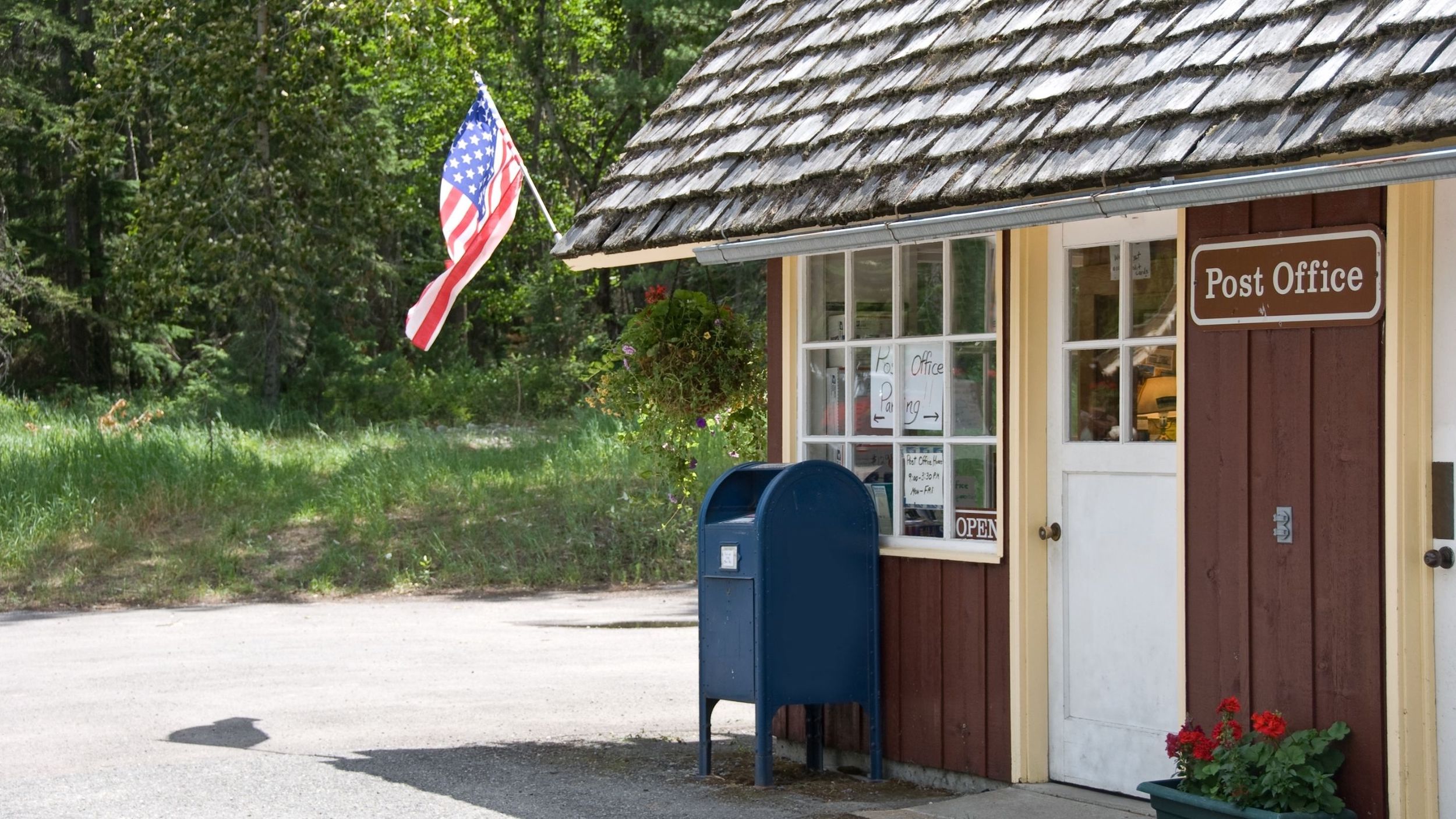 Rural town post office with blue box in front and american flag flying.