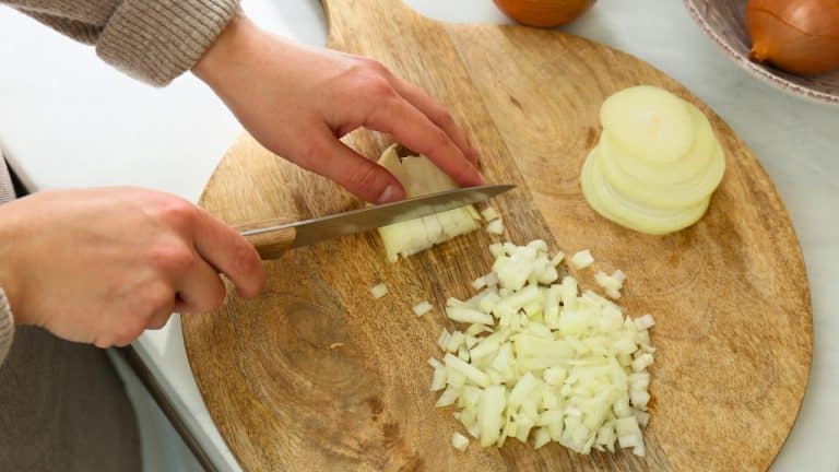 Knife slicing through white onions, dicing them on wooden cutting board