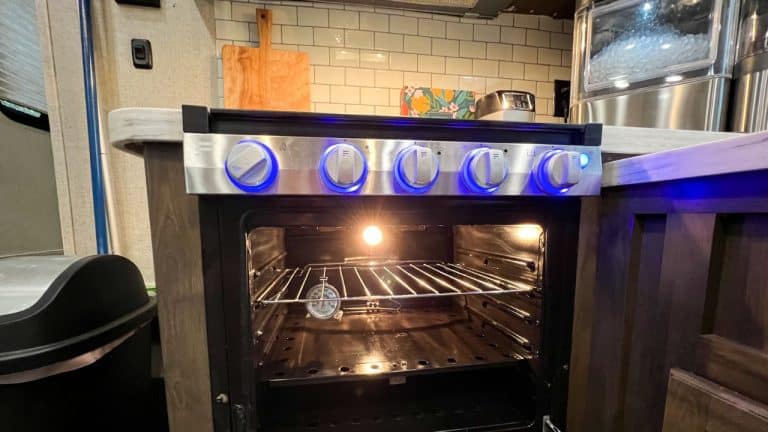 RV oven and cooktop with oven door open. Thermometer hanging from rack.