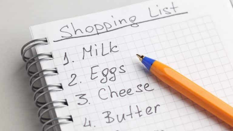 Shopping list written on spiral bound notebook. Pen is resting on top of the page.