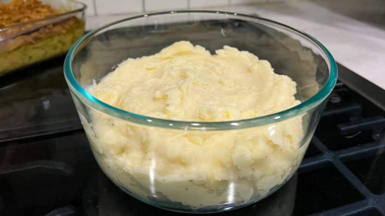 Clear bowl filled with creamy mashed potatoes sitting on black stovetop